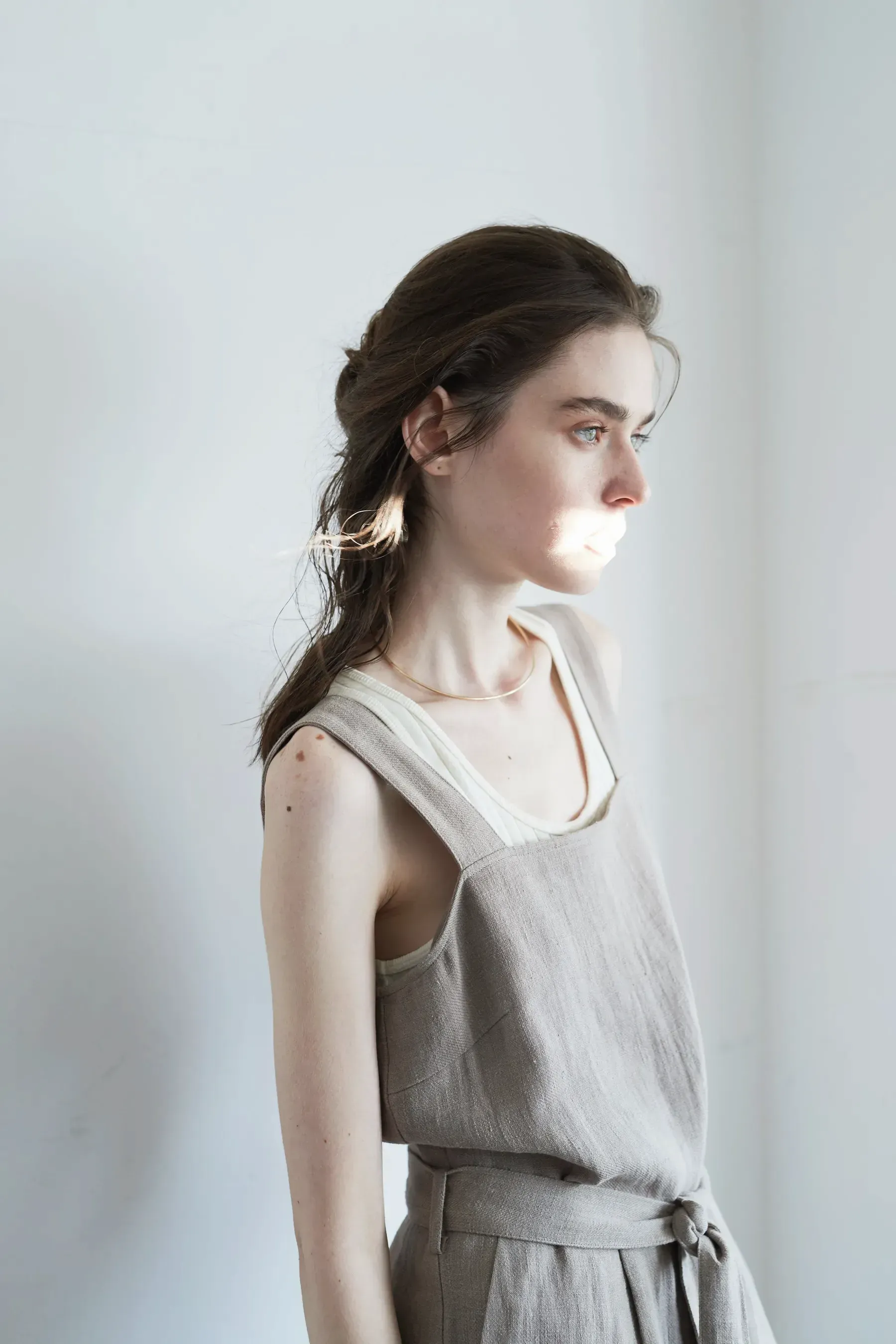 A woman in the Ash Linen Pinafore Dress, turned to the light