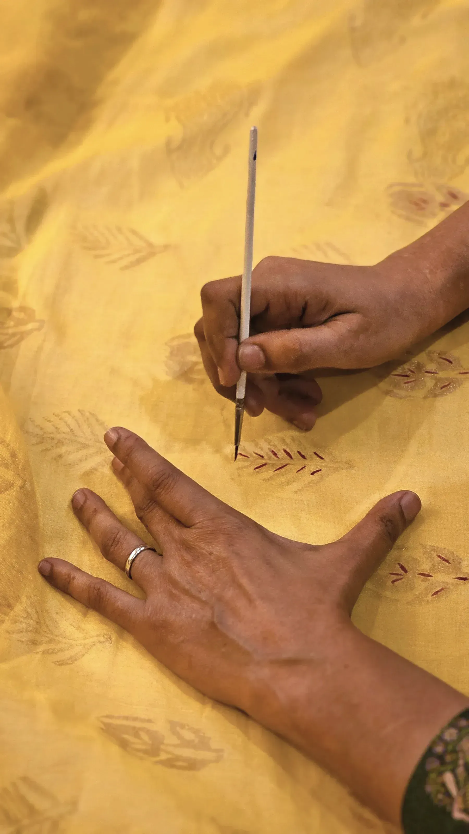 A hand marking a motif on turmeric yellow cotton