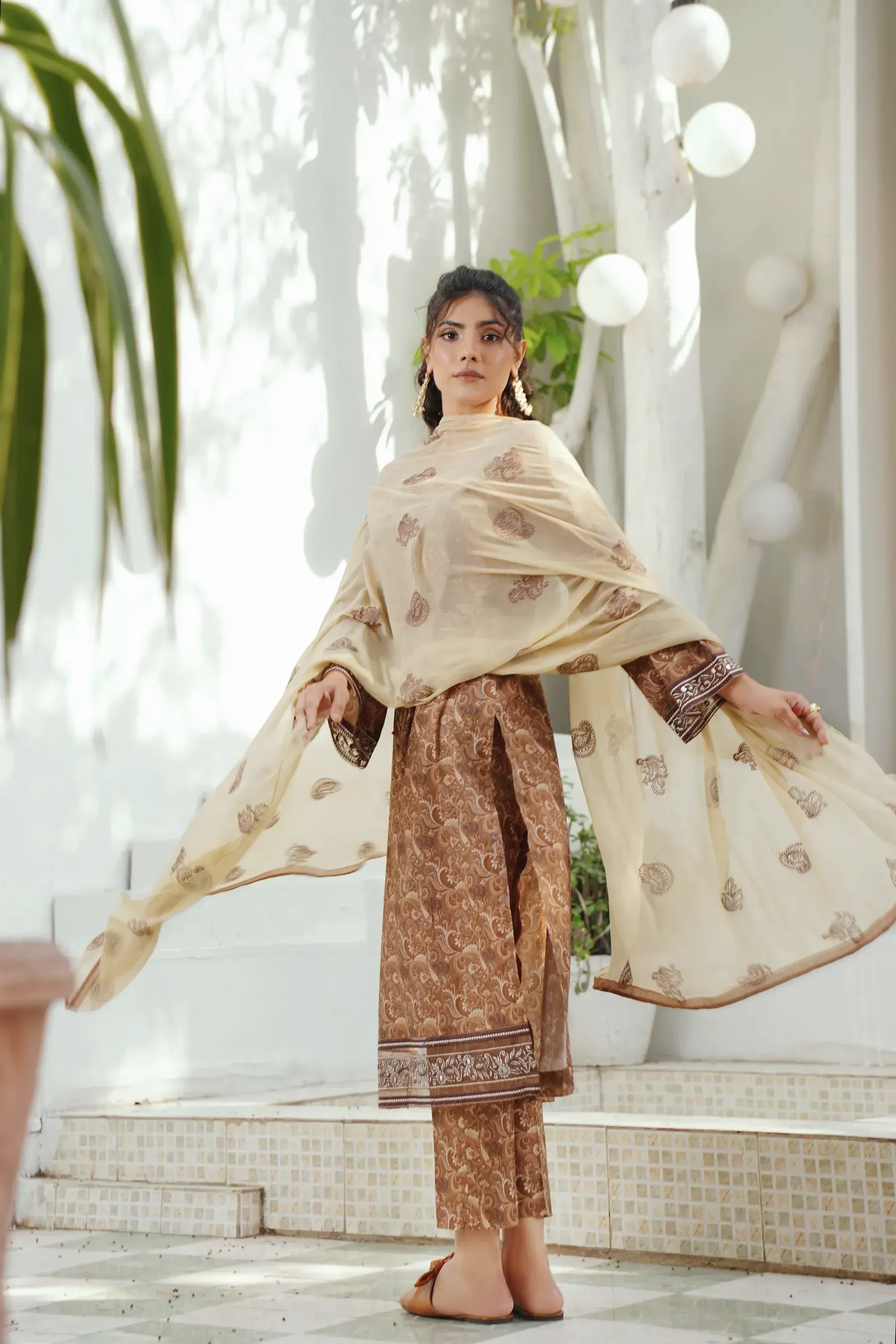 A woman swinging a printed mulmul dupatta in a white room