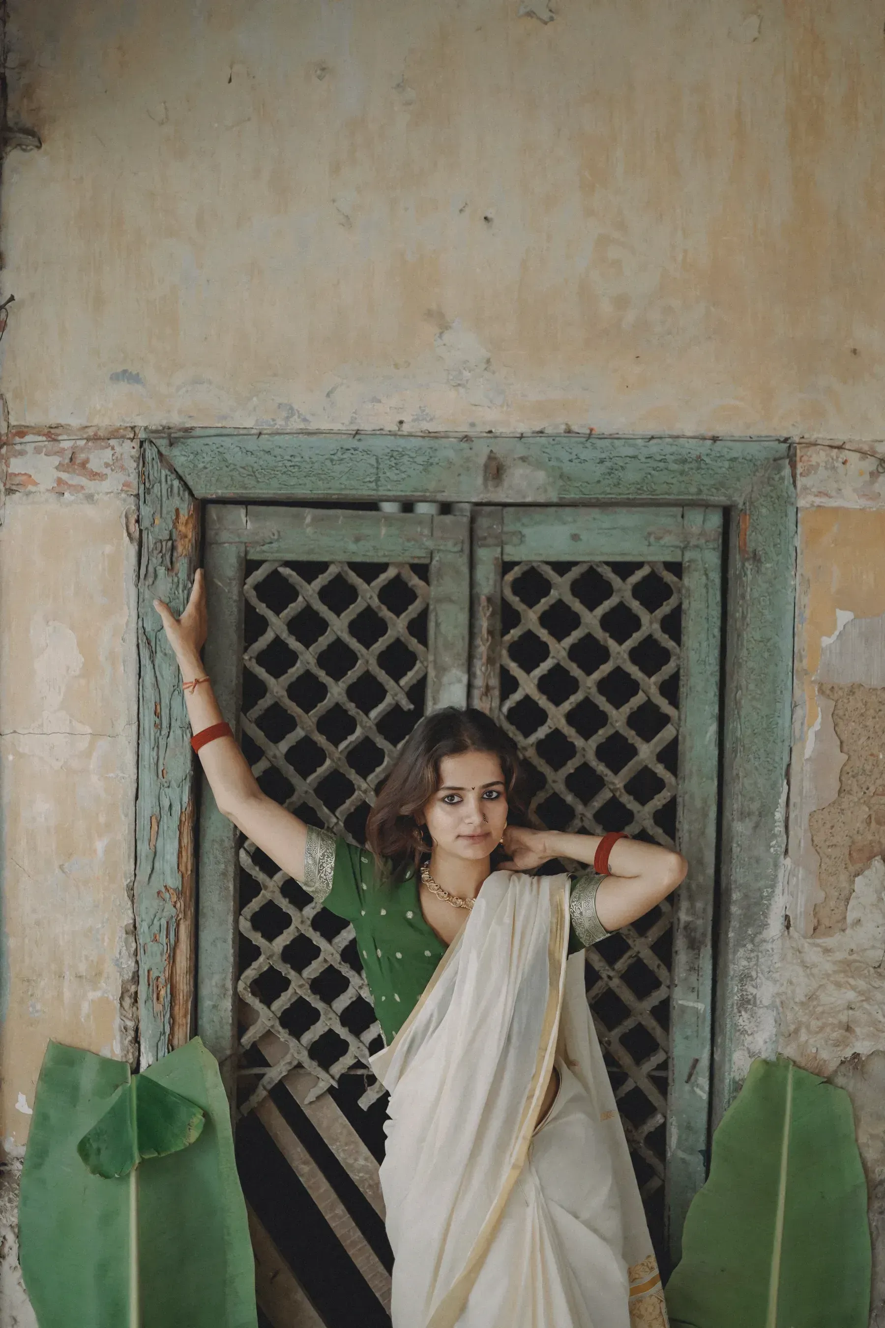 A woman in an ivory cotton saree with a green blouse at an old window