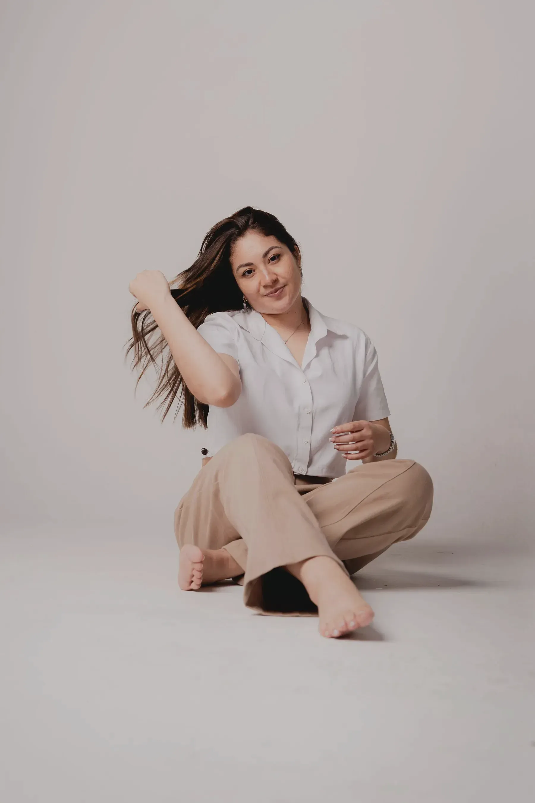 A woman sitting on the floor in a white mulmul shirt and oat linen trousers