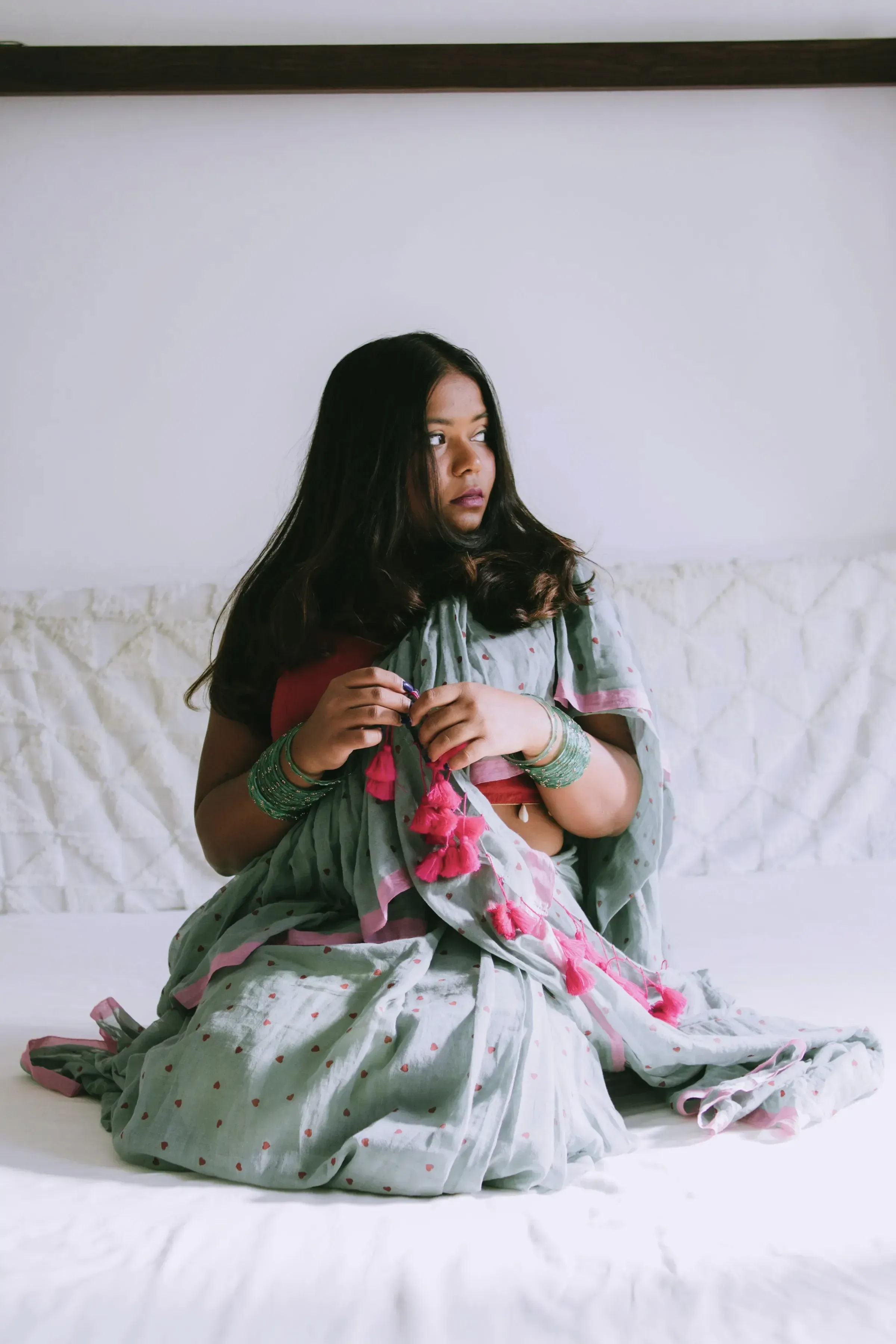 A woman seated on white sheets in the Sage Dabu Mulmul Saree