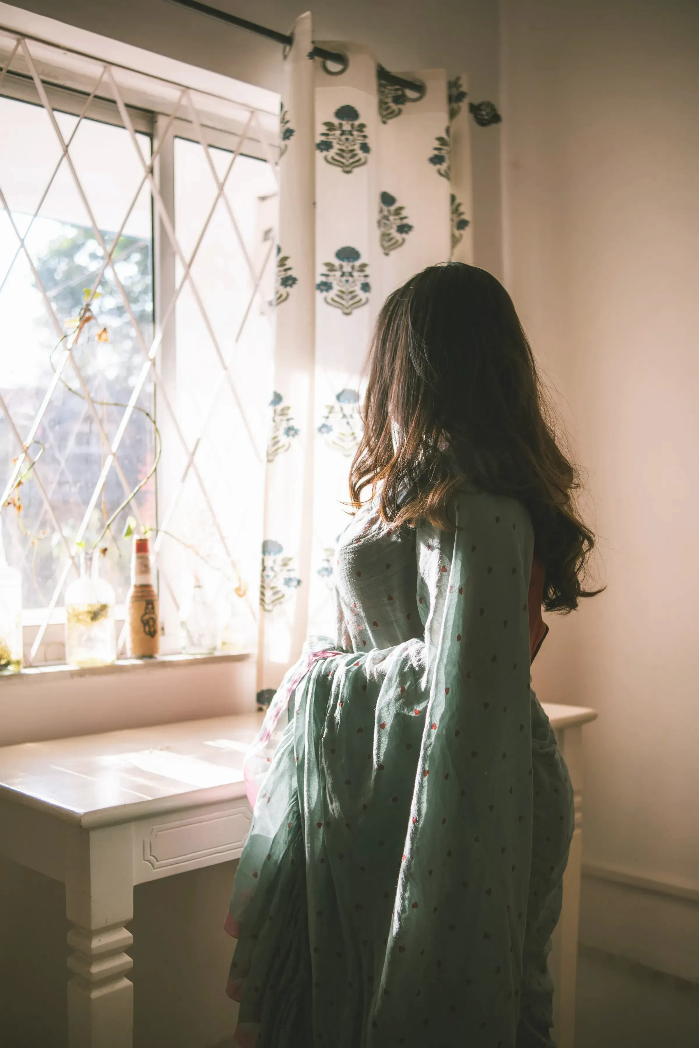 A woman in a sage mulmul saree by a window in afternoon light