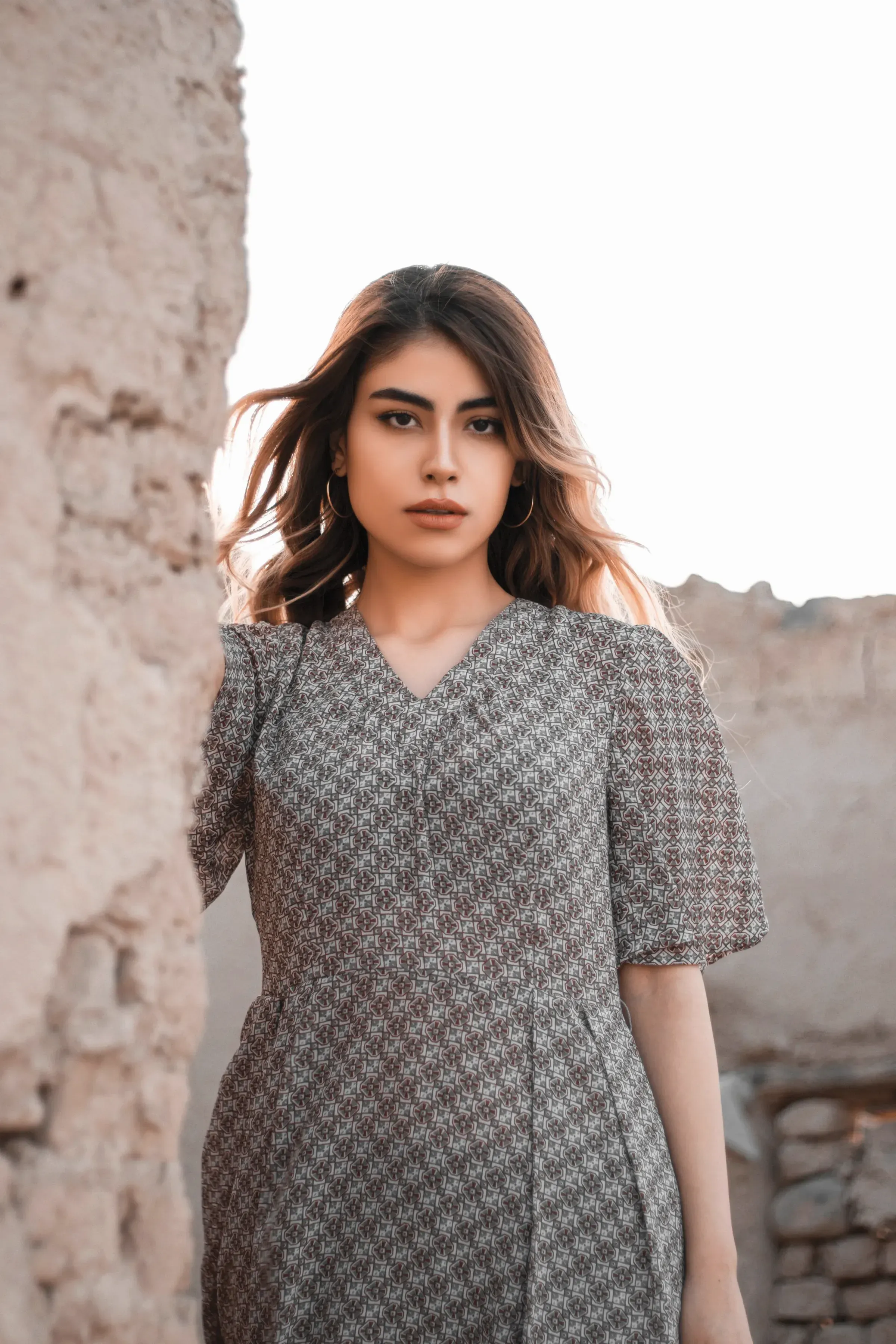A woman in the Slate Bagru Midi Dress standing by an old mud wall